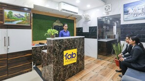 A reception desk with a 'fab hotels' sign, a receptionist, and two guests seated. - Fabhotel Shaurya Inn (Lucknow)