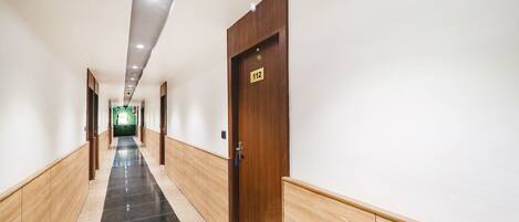 A long, narrow hallway with a wooden door labeled "112" on the right. The hallway has a tiled floor with a black and beige pattern.