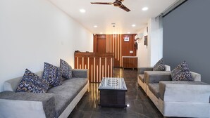 A modern lobby with a reception desk, two sofas with patterned cushions, a coffee table, and a ceiling fan. - FabHotel The Royal - Near Yamuna Sports Complex (New Delhi)