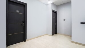 A hallway with two black doors, each marked with a number. The walls are light grey, and the floor is tiled. - FabHotel The Royal - Near Yamuna Sports Complex (New Delhi)