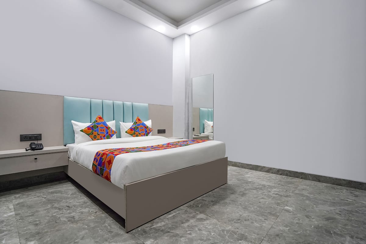 A modern hotel room with a large bed, a bedside table, a nightstand, a mirror, and a wall-mounted light fixture.