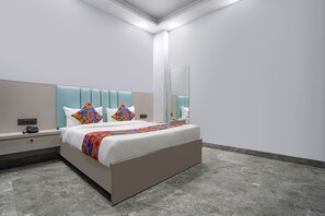 Une chambre d’hôtel moderne avec un grand lit, une table de chevet, une commode, un miroir et un luminaire fixé au mur.