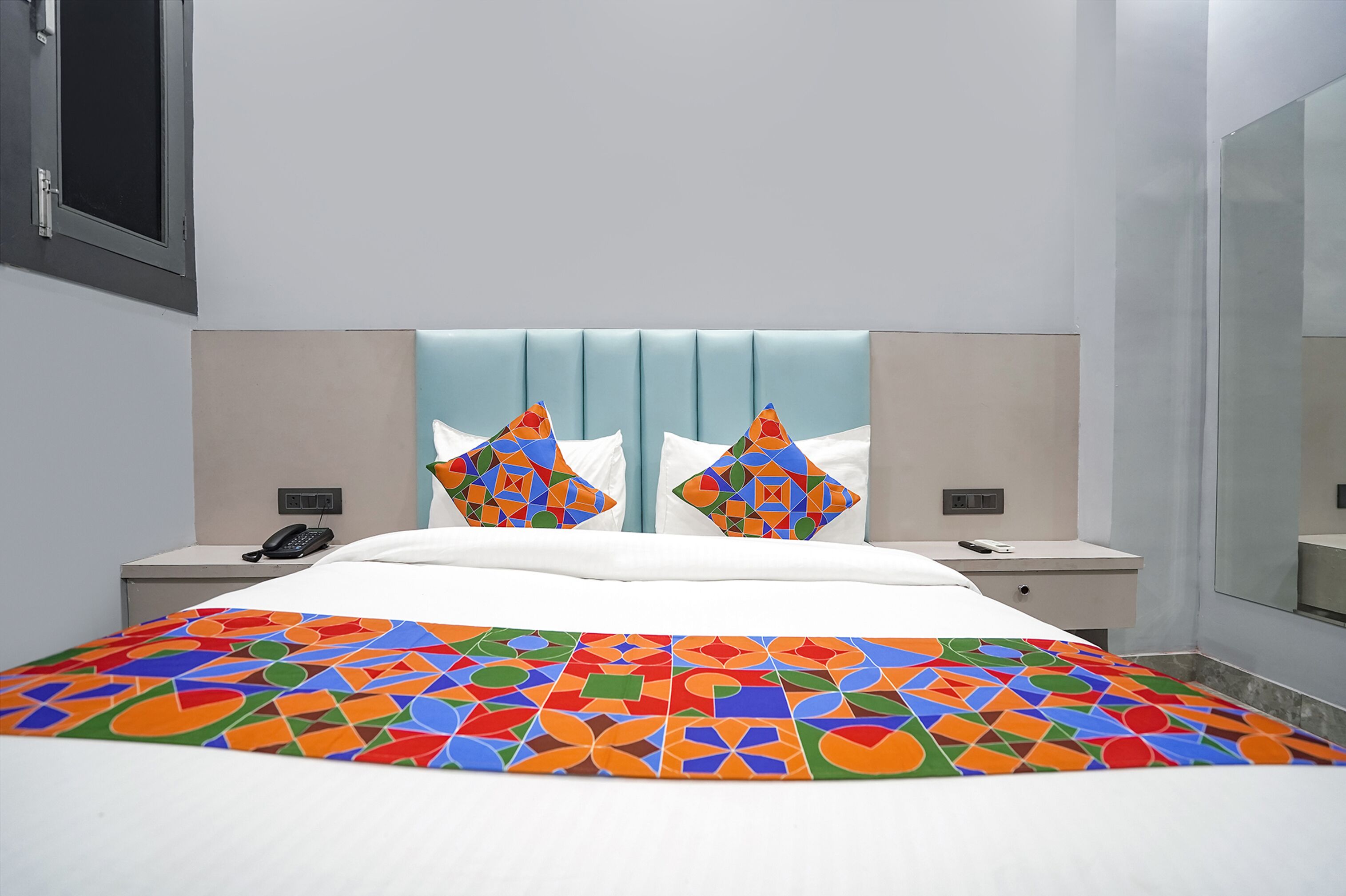 Une chambre d’hôtel moderne avec un grand lit, deux tables de chevet, un téléphone et un miroir.