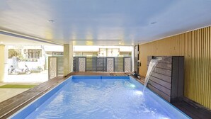 An indoor swimming pool with a wooden deck, a water feature, and a view of the outside. - Fabhotel Hari Om Inn (Rishikesh)