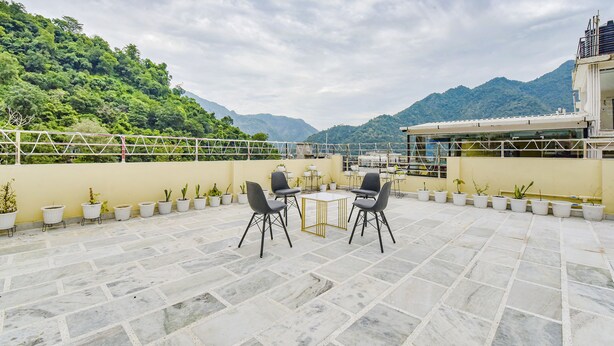 A terrace with two tables and chairs, potted plants, and a view of mountains. - Fabhotel Hari Om Inn (Rishikesh)