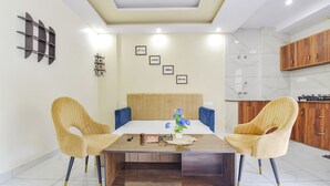 A modern dining area with a wooden table, two yellow chairs, and a decorative vase. - Fabhotel Hari Om Inn (Rishikesh)