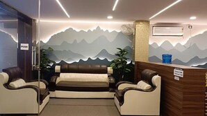 A reception area with a reception desk, two sofas, a wall mural, and a push button. - Fabhotel Sprinkle Stay (Hyderabad)