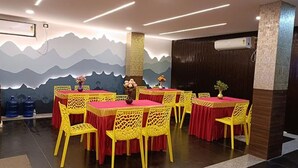 A dining area with tables and chairs, a decorative wall with mountain designs, and water dispensers. - Fabhotel Sprinkle Stay (Hyderabad)