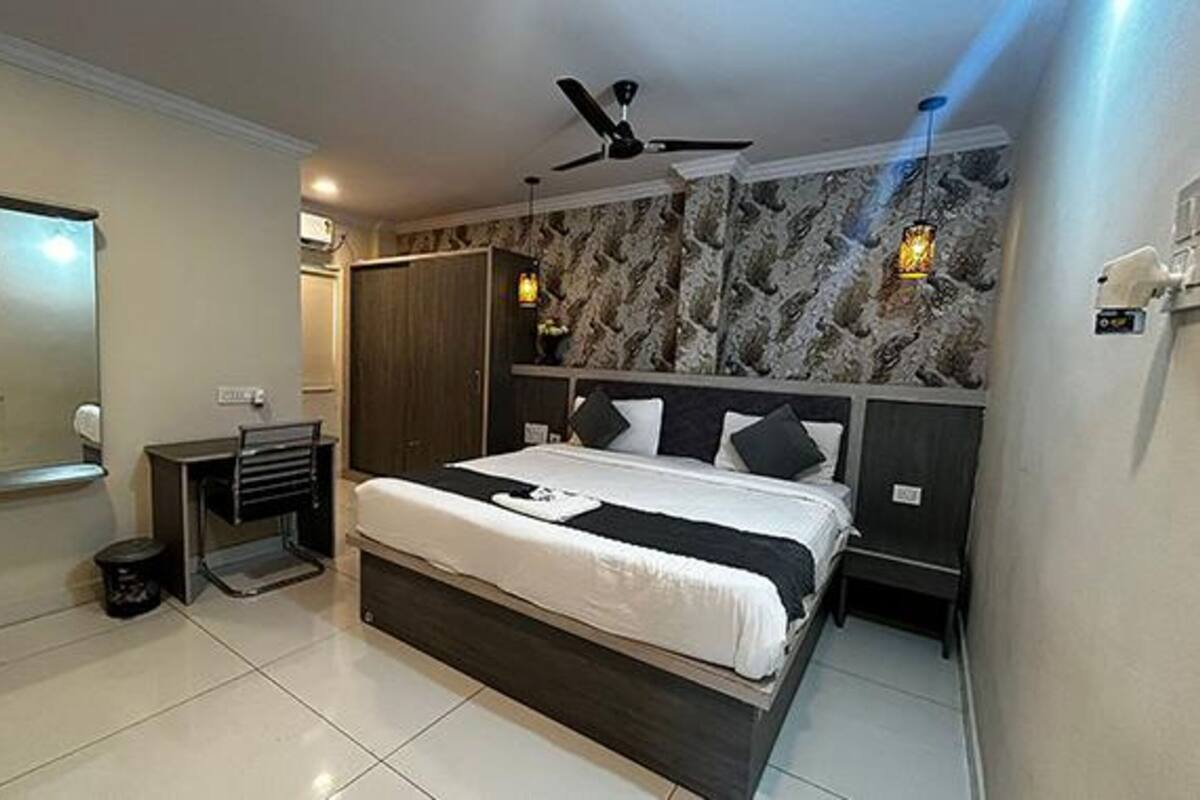 Un dormitorio moderno con una cama grande, un ventilador de techo, una pared con diseño de mármol y un pequeño escritorio con silla.