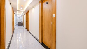 A long, narrow hallway with wooden doors and a marble floor. - Fabhotel Crystal I (Gandhinagar)