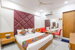 A hotel room with a bed, a desk, a chair, a wardrobe, and a ceiling fan. - Fabhotel Crystal I (Gandhinagar)