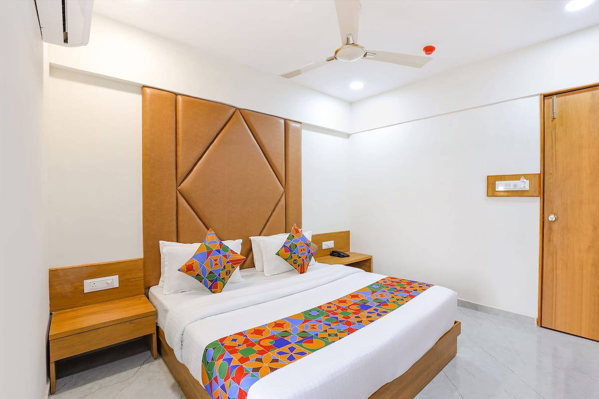 Une chambre d’hôtel moderne avec un grand lit, une tête de lit en bois, des tables de chevet et un ventilateur de plafond.