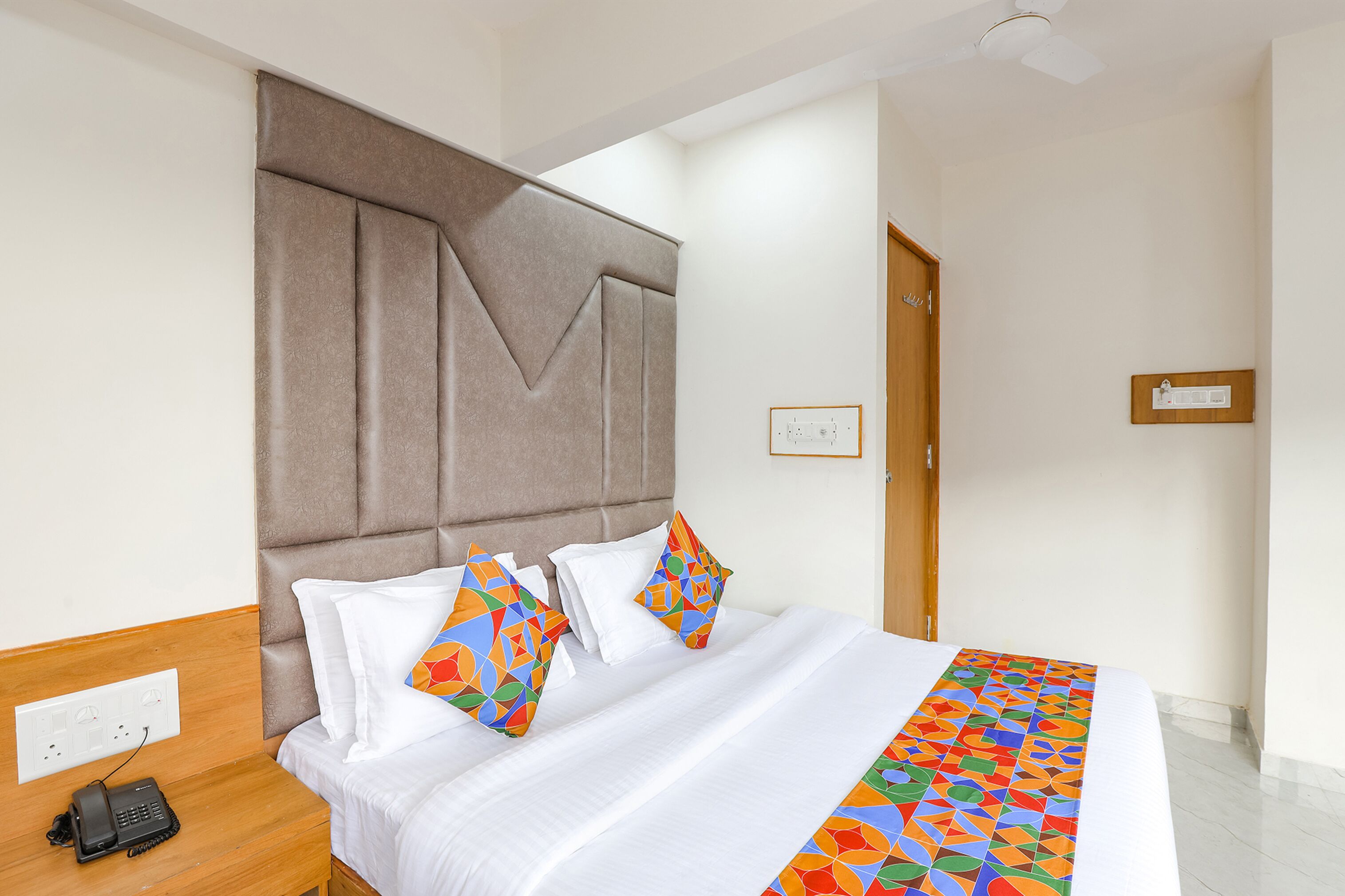Une chambre d’hôtel avec un grand lit, une tête de lit en bois, un téléphone sur la table de chevet et une prise électrique au mur.