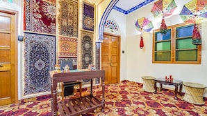 A room with a patterned carpet, a wooden bench, and a traditional woven stool. - Fabhotel Prism Homestay (Jaipur)