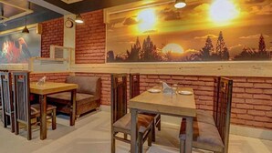 Un restaurant aux murs de briques, aux tables et chaises en bois, et orné d’une fresque représentant un coucher de soleil.