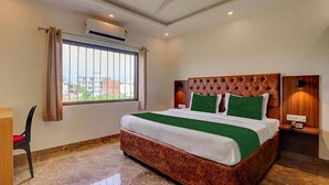 Une chambre d’hôtel avec un grand lit, une fenêtre avec des rideaux, un appareil de climatisation et une chaise.