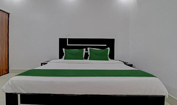 A neatly made bed with a white and green bedspread, a black headboard, and two green pillows.