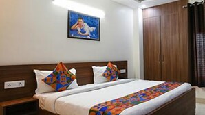 Un lit bien fait, avec une couverture colorée et des oreillers, un ventilateur de plafond, une armoire en bois et un tableau accroché au mur.