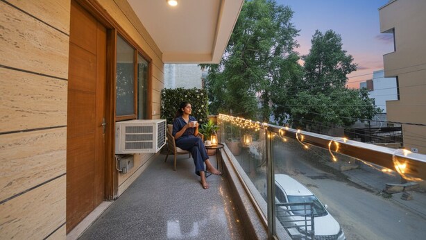 Un balcon avec une personne assise, une table avec une plante et des guirlandes lumineuses.
