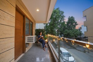 A balcony with a person sitting, a table with a plant, and string lights. - FabHotel Muktinath (Gurugram)