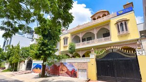 Un edificio tradicional con fachada amarilla, una reja negra y un mural que representa una escena histórica.