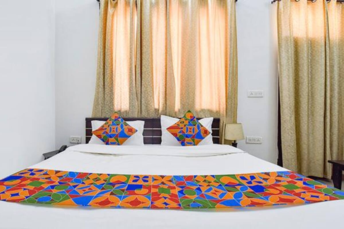 A hotel room with a large bed, two pillows with colorful geometric patterns, and beige curtains.