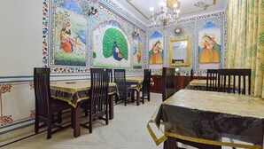 Un comedor con decoración tradicional, que incluye paredes con diseños y una araña. Mesas y sillas dispuestas para comer.