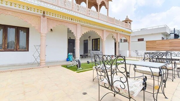 Un patio con mobiliario exterior, un pequeño jardín y un edificio de arquitectura tradicional.