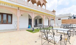 Un patio con mobiliario exterior, un pequeño jardín y un edificio de arquitectura tradicional.