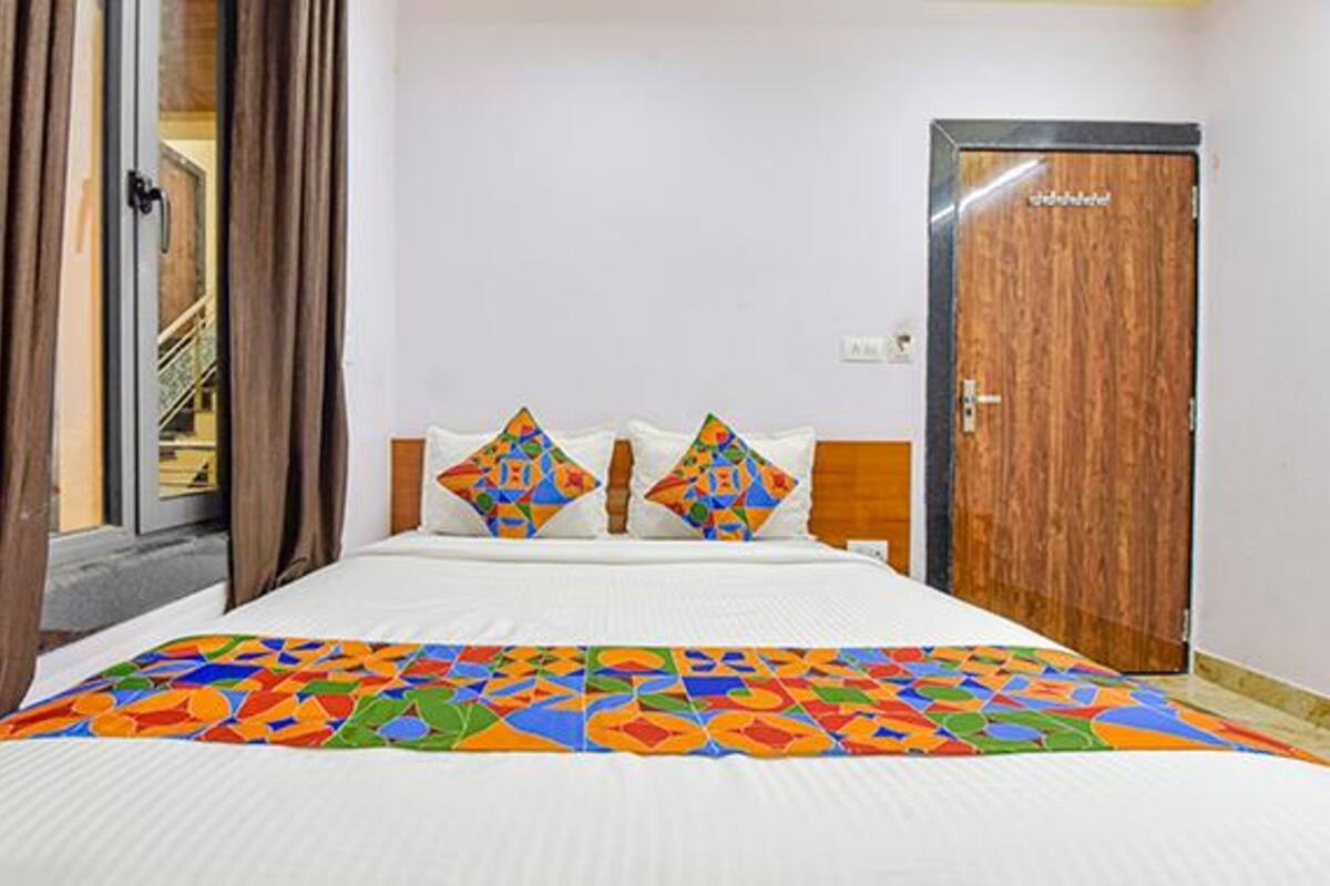 A hotel room with a bed, two pillows, a wooden door, and a window with curtains.