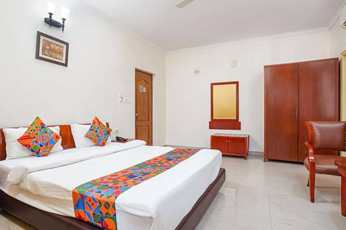 A hotel room with a large bed, a wooden wardrobe, a desk, and a chair.