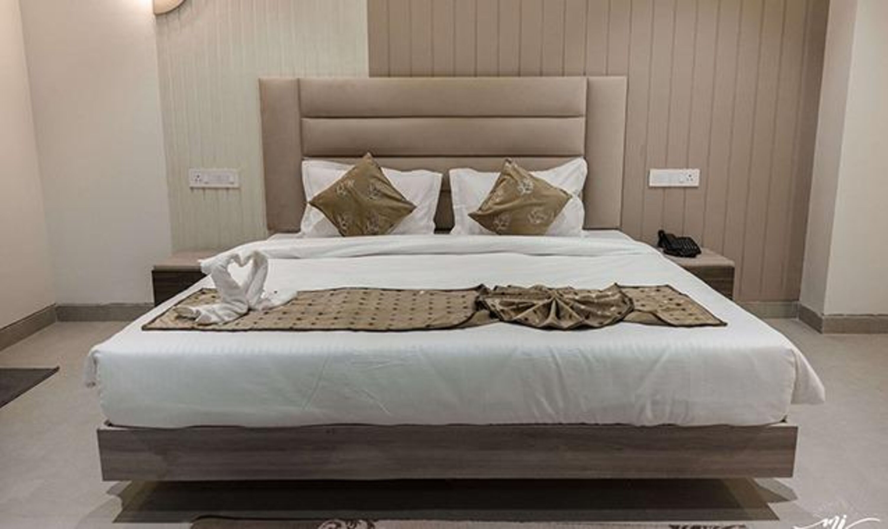 A bed with a headboard, two pillows, a blanket, and a heart-shaped towel on the bed.
