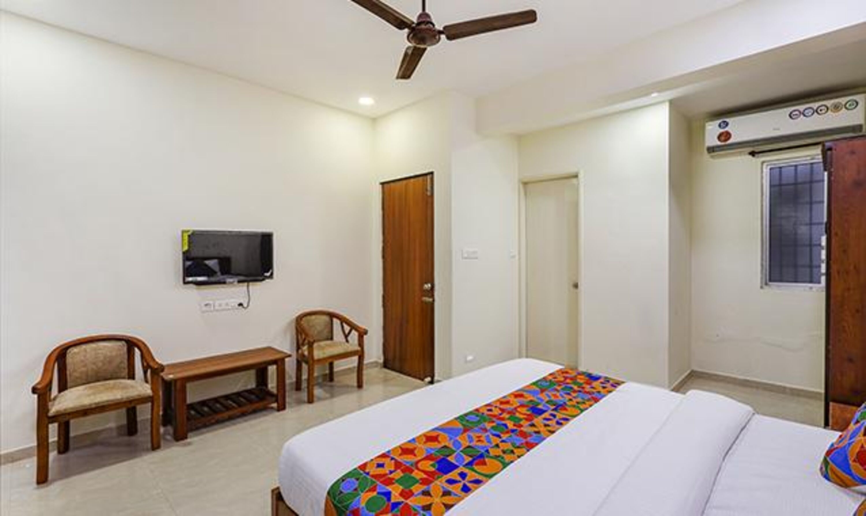 A hotel room with a bed, a desk, two chairs, a television, and a ceiling fan.