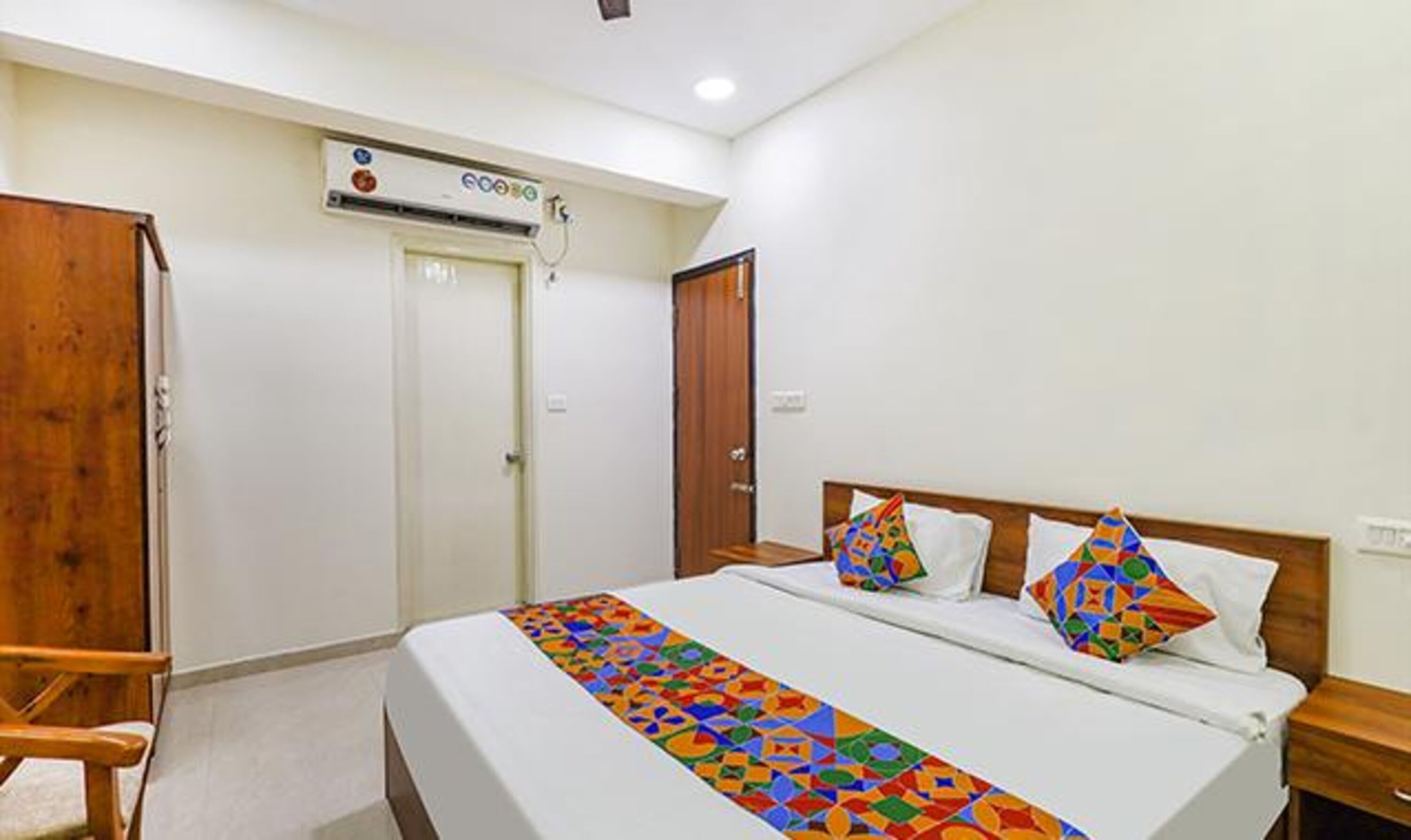 A hotel room with a bed, a wooden chair, a desk, and a wardrobe.