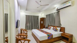 A bedroom with a bed, a desk, a chair, a wardrobe, and an air conditioning unit. - Fabhotel De Luxe (Chennai)