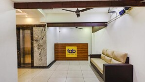 A reception area with a wooden reception desk labeled "fab hotels," a beige sofa, a ceiling fan, and a marble wall. - Fabhotel De Luxe (Chennai)