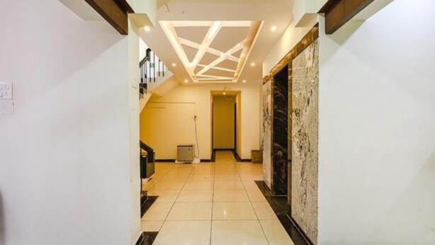 A hallway with a geometric ceiling design, a tiled floor, and a stone wall on the right. - Fabhotel De Luxe (Chennai)