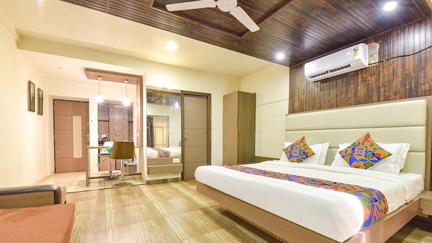 Une chambre d’hôtel avec un grand lit, un bureau, une chaise, une armoire et un ventilateur de plafond.