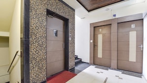 Un espace d’ascenseur moderne avec un mur carrelé, une moquette rouge et une porte en bois portant une plaque avec un numéro.