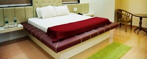 A hotel room with a large bed, a nightstand with water bottles, a green rug, and a wooden chair.
