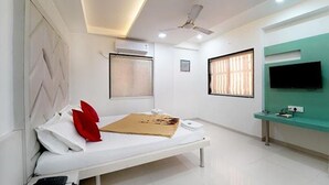 Un dormitorio moderno con cama, ventilador de techo, equipo de aire acondicionado, televisor y ventana con persianas.