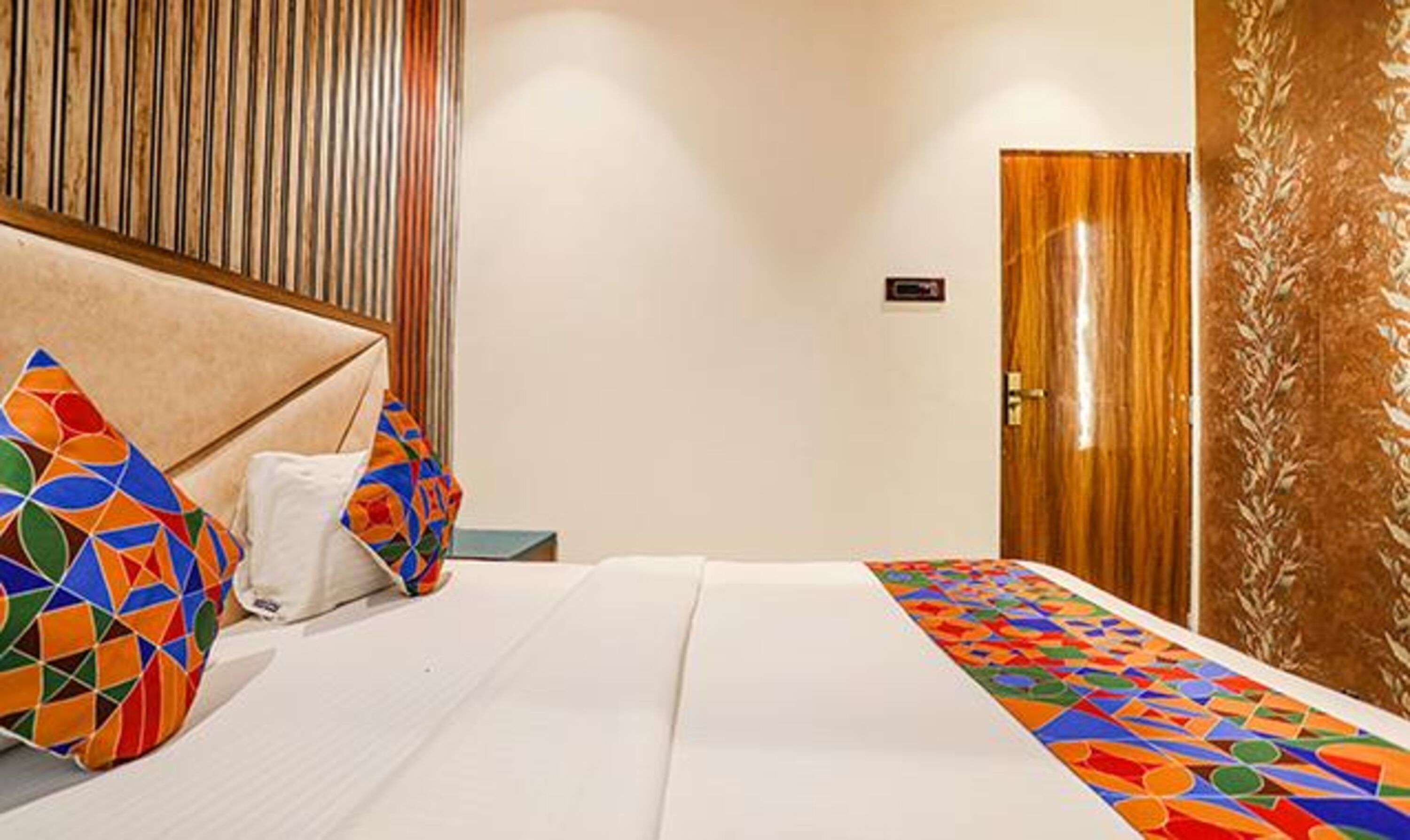 Une chambre d’hôtel avec un lit, des oreillers, une tête de lit en bois, une porte et un mur orné de lignes verticales.