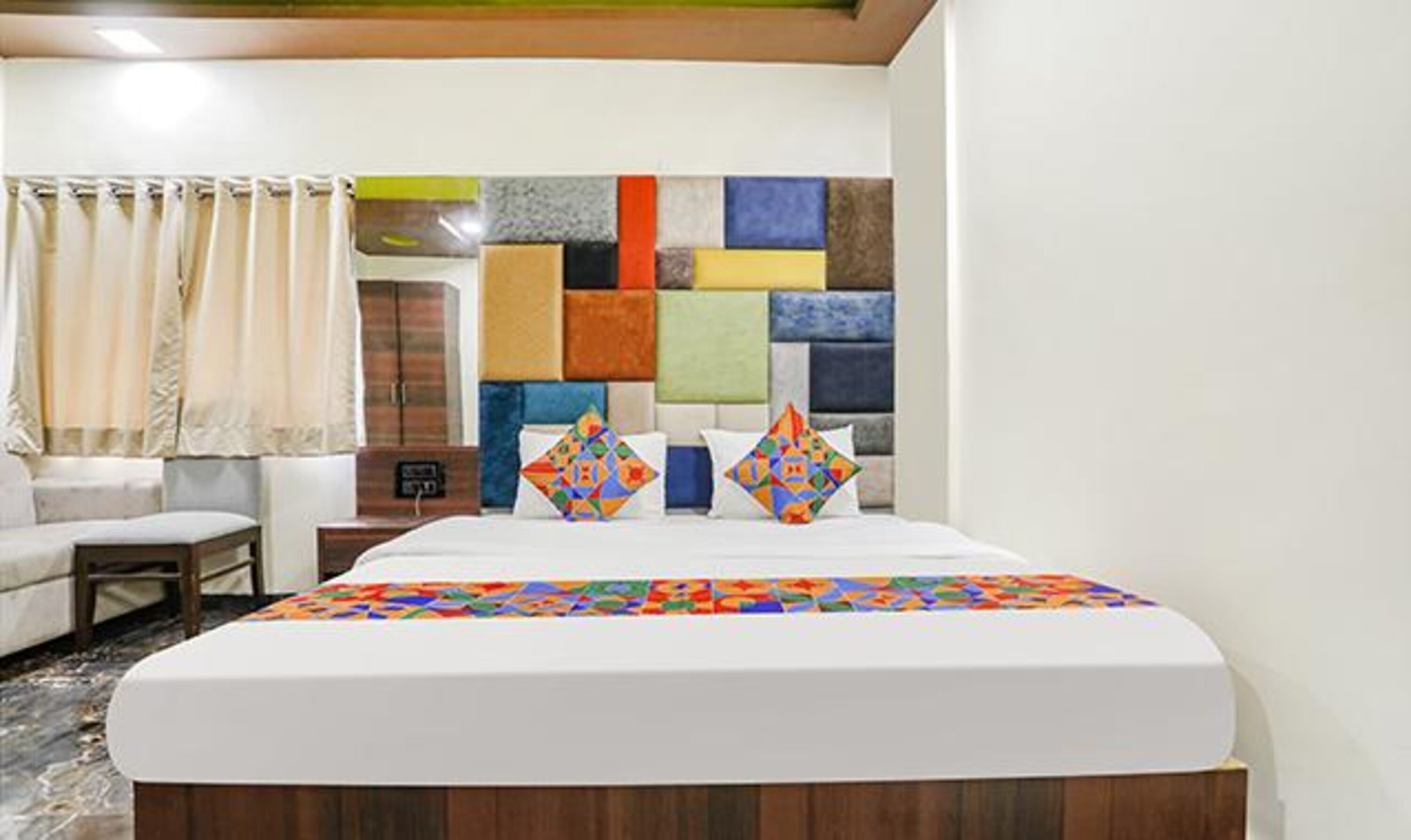 Una habitación de hotel con una cama grande, una mesita de noche, un cabecero de madera y un panel de pared colorido.