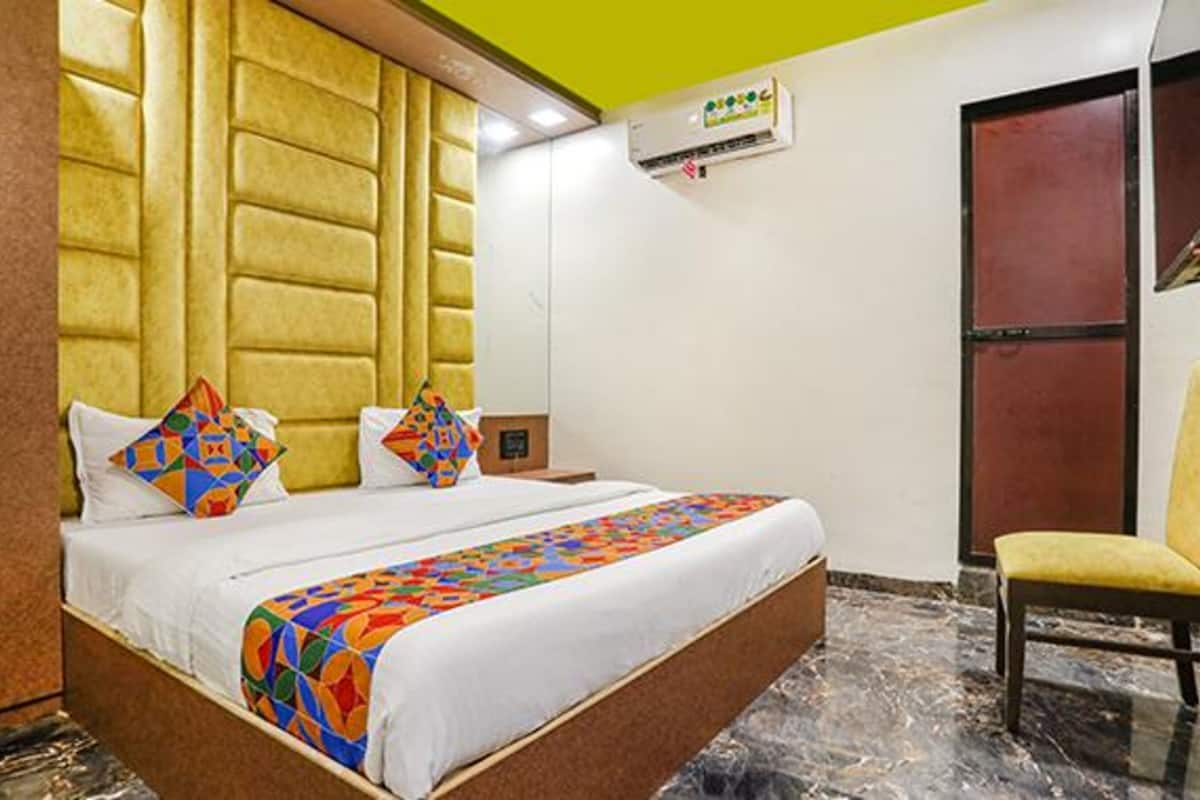 A hotel room with a bed, a chair, a wall-mounted air conditioner, and a door.