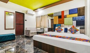A hotel room with a bed, a sofa, a mirror, and a window with curtains. - Fabexpress Versova Residency (Mumbai)