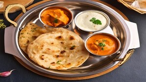 Un plato de acero inoxidable con pan naan, pollo a la mantequilla y raita.