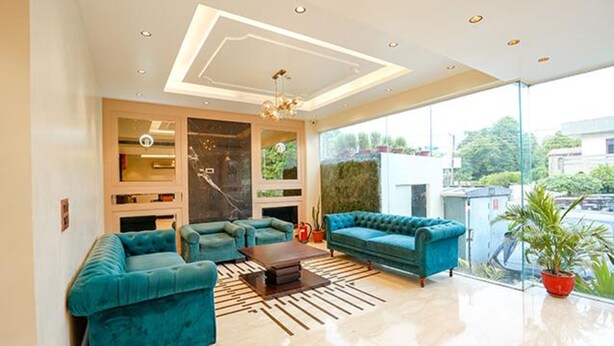 A modern living room with teal sofas, a coffee table, and a large window offering a view of the city. - FabHotel Prime Tushar Elegant (Ghaziabad)