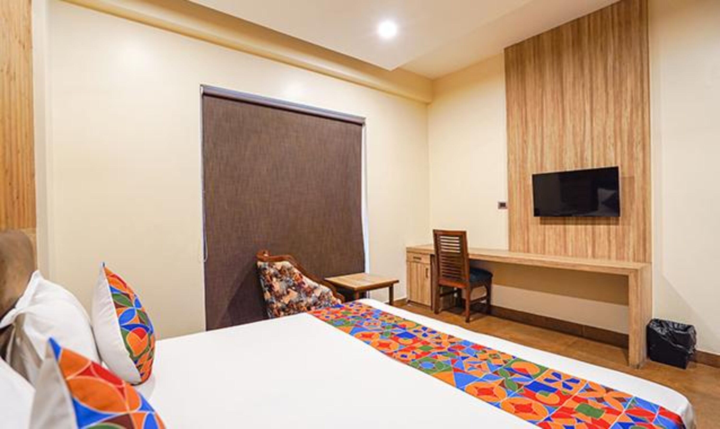 A hotel room with a bed, a desk, a chair, a TV mounted on the wall, and a door.