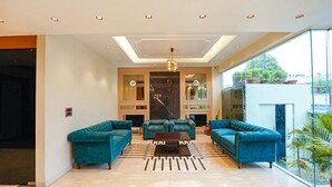 A spacious living room with a modern design, featuring a large sofa set, a chandelier, and a large window offering a view of the outdoors. - FabHotel Prime Tushar Elegant (Ghaziabad)