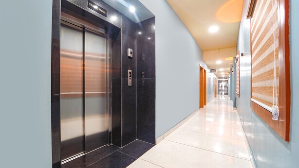 Un couloir moderne avec un ascenseur noir, une porte en bois et un panneau indiquant le rez-de-chaussée.